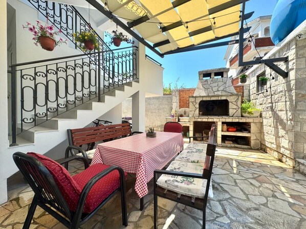 Un patio al aire libre con una mesa y sillas, suelo de piedra, una escalera y un horno de ladrillo.