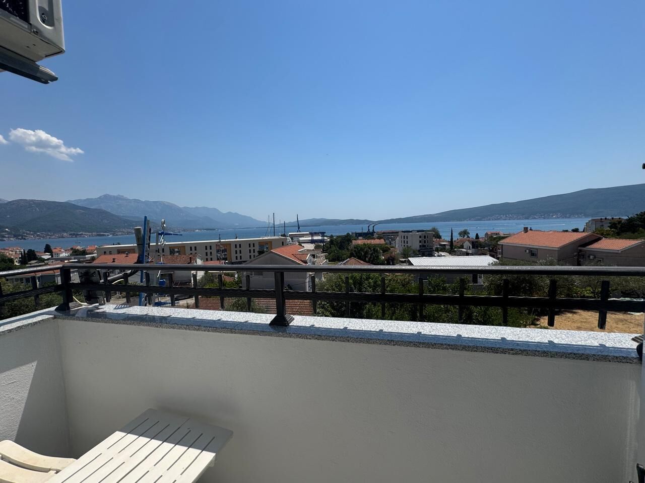 A balcony with a view of a coastal town, buildings, and mountains.