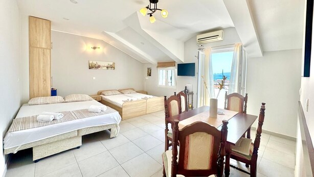 A bedroom with two beds, a dining table with chairs, a ceiling fan, and a view of the sea. - Apartments Janda Bijela (Bijela)