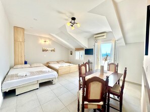 Un dormitorio con dos camas, una mesa de comedor con sillas, un ventilador de techo y vista al mar.