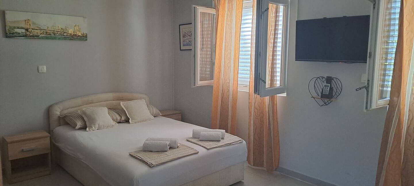 A bedroom with a bed, two nightstands, a TV mounted on the wall, and a window with curtains.