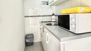 A compact kitchen with white cabinets, a stainless steel sink, a microwave, and a trash bin. - Apartments Janda Bijela (Bijela)