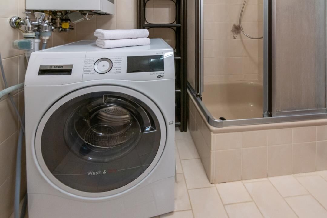 Een Bosch wasmachine met bedieningspaneel en een transparante deur, in een badkamer met douche.