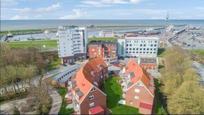 Un hotel con varias edificaciones, incluyendo una gran estructura blanca y varias casas con tejados rojos, ubicado cerca de un puerto y un puente.