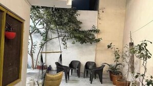 Een smalle gang met een hangstoel, verschillende potplanten en enkele stoelen.