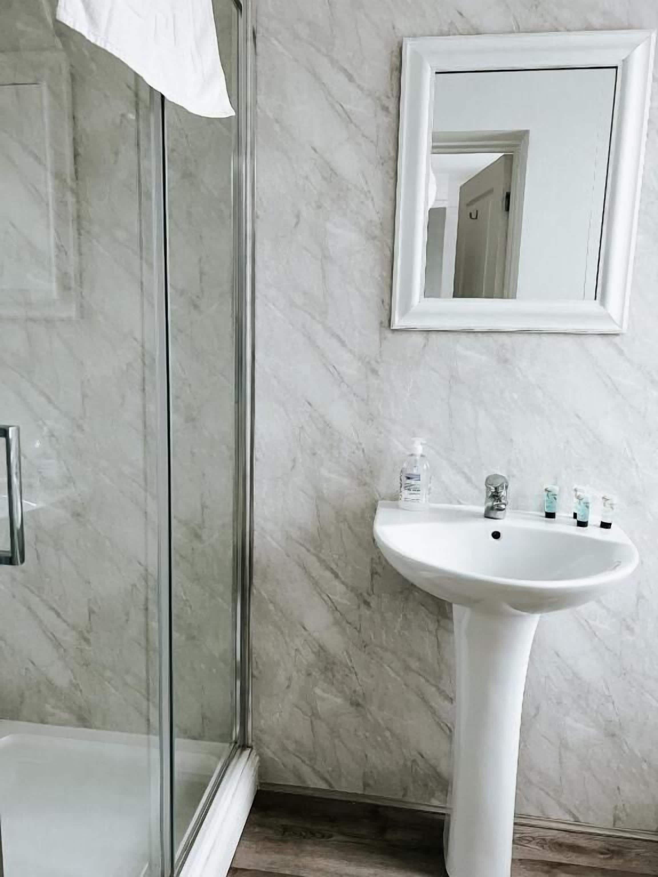 A bathroom with a glass shower enclosure, a white sink with a marble countertop, and a mirror on the wall.