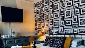 Quarto com cama, cômoda, televisão e parede decorada com quadros.