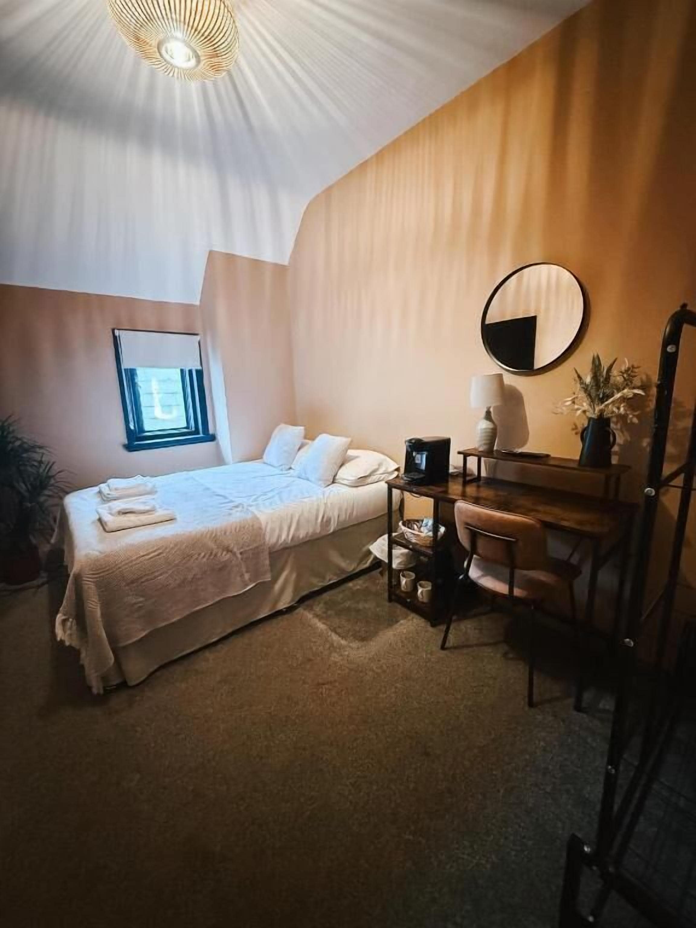 Un dormitorio con cama, mesita de noche, lámpara y ventana.