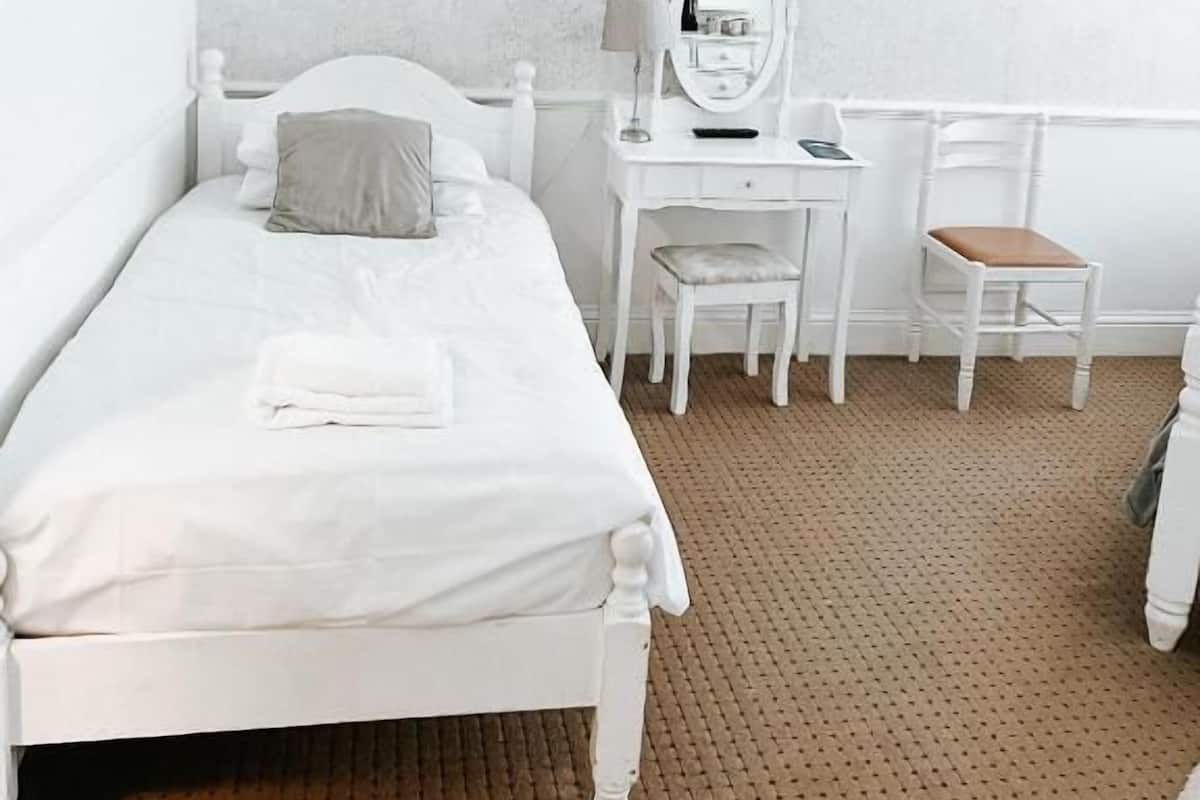 A white bed with a pillow, a small desk with a mirror, and a chair.