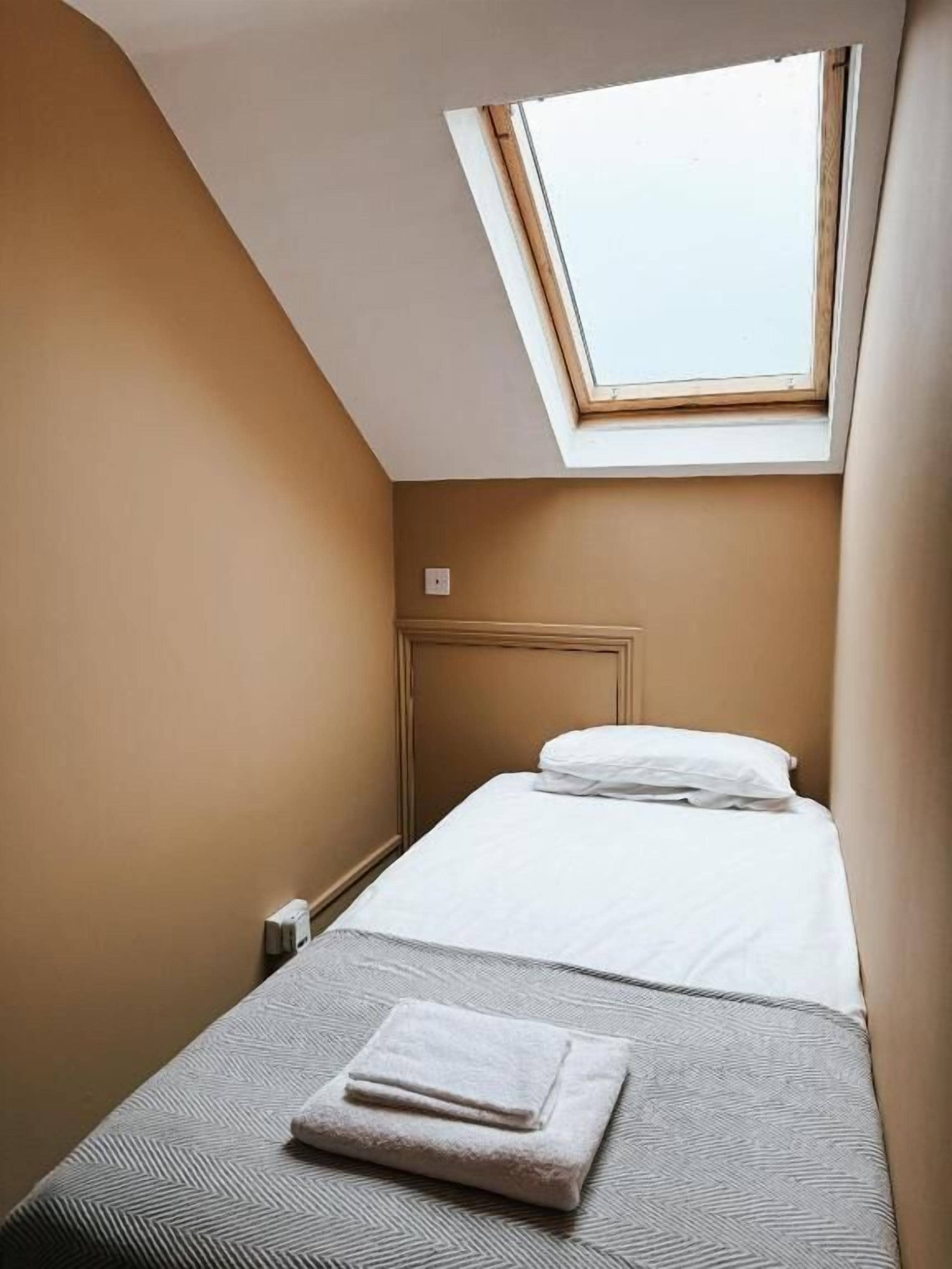 A small, single-bed room with a sloped ceiling and a skylight.