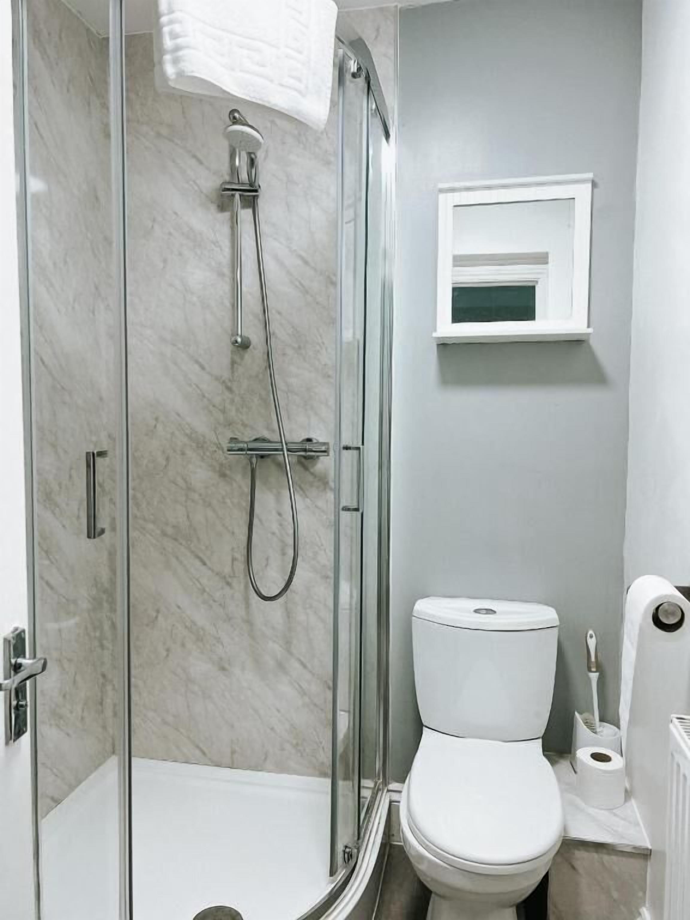 Un baño con ducha acristalada, inodoro blanco y una pequeña ventana sobre el inodoro.