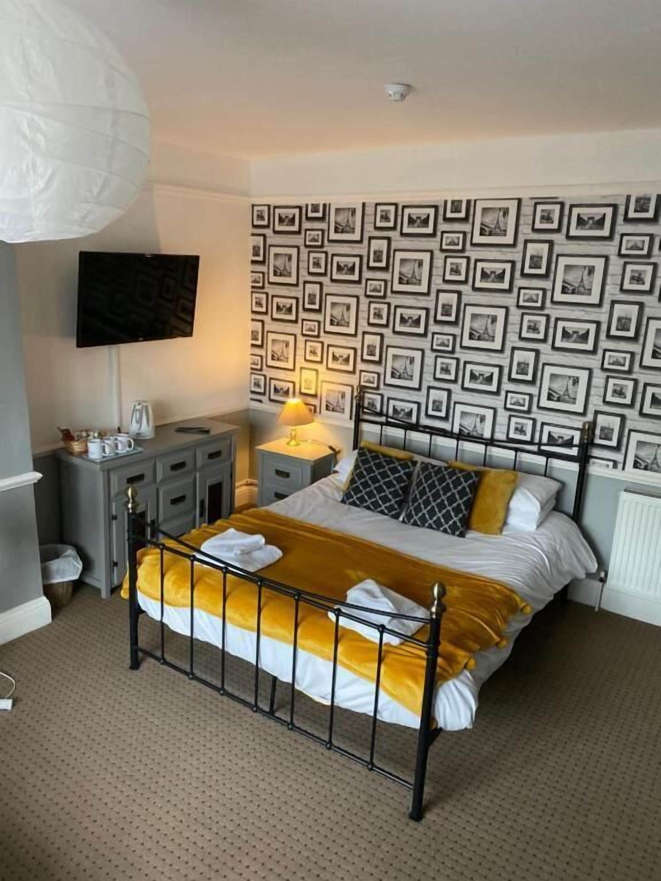 A bedroom with a bed, bedside tables, a lamp, a TV, and a patterned wall.