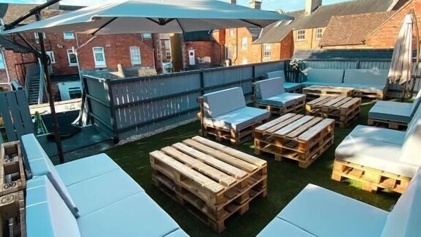 Terraço no telhado com áreas de estar, uma pérgula e vista dos edifícios ao redor.