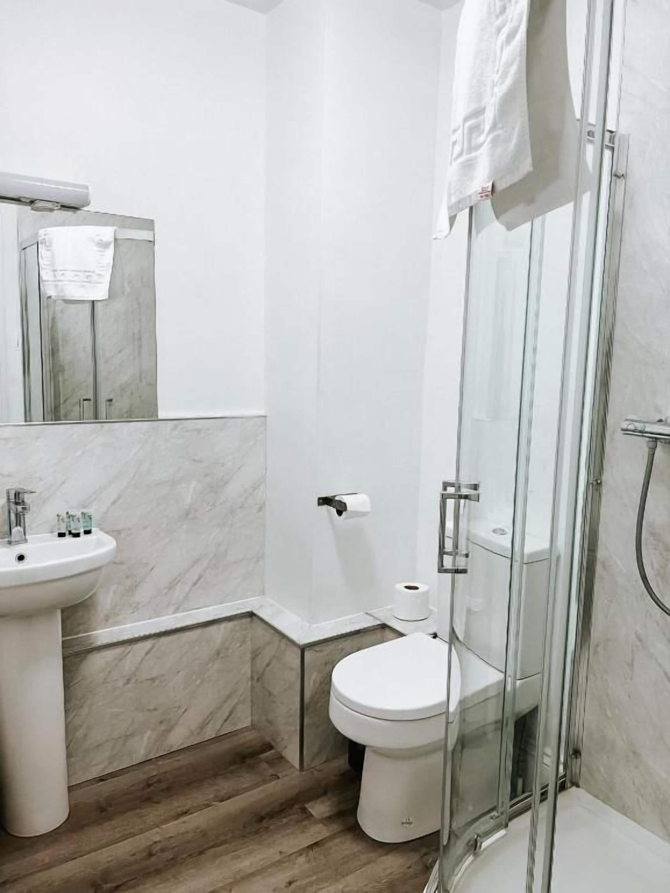 A modern bathroom with a marble sink, toilet, and glass shower enclosure.