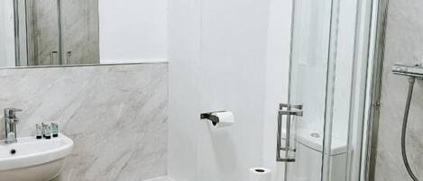 A modern bathroom with a marble sink, toilet, and glass shower enclosure.