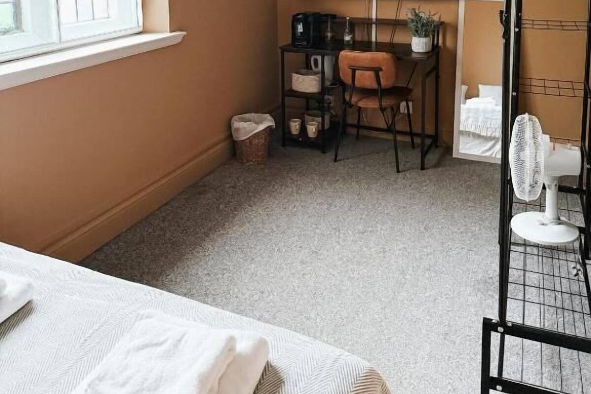 A compact room with a television mounted on the wall, a small desk with a chair, and a radiator.