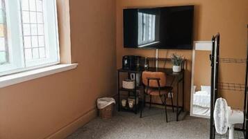 Une pièce de taille modeste, dotée d’un téléviseur fixé au mur, d’un petit bureau avec une chaise et d’un radiateur.