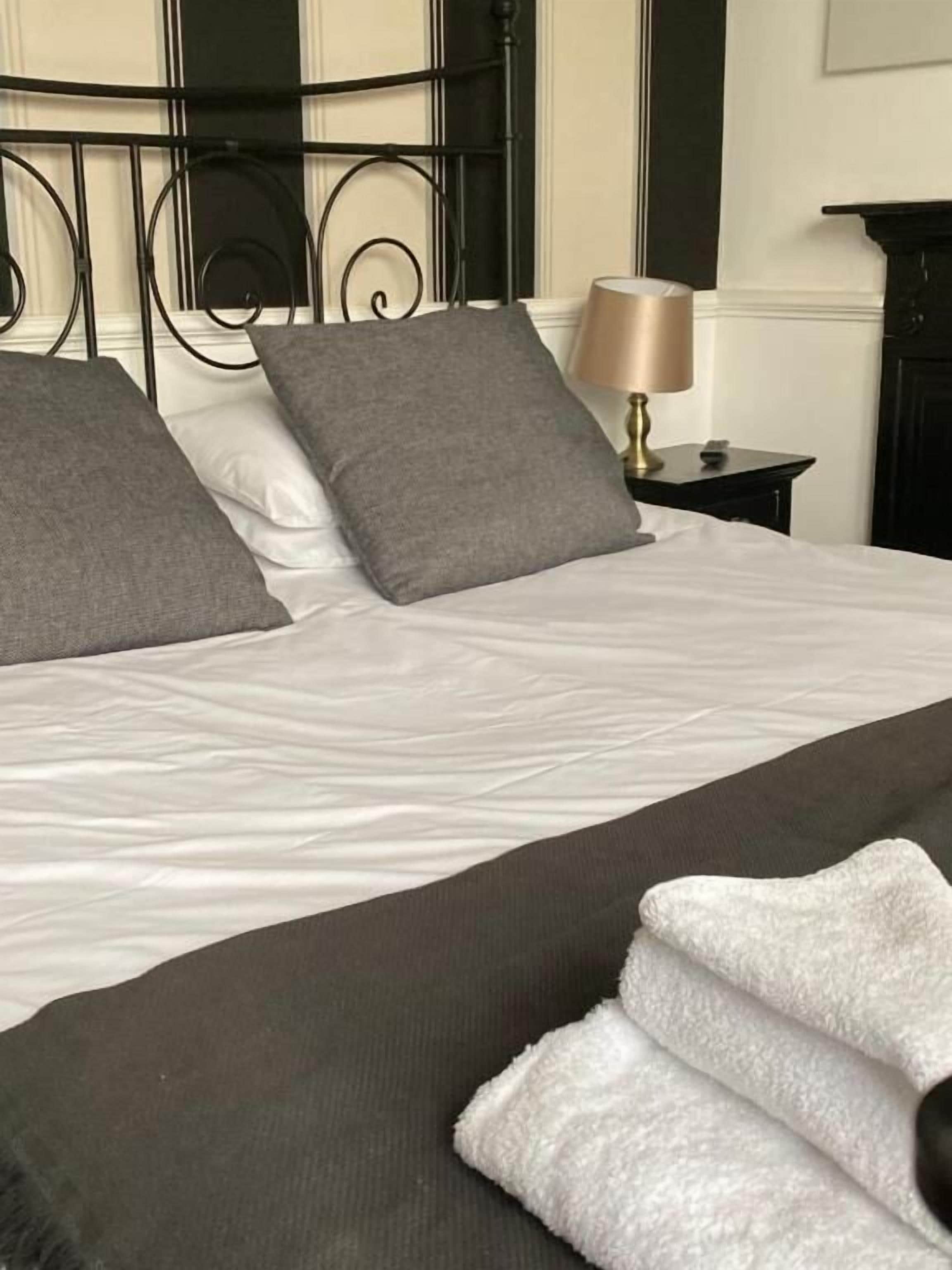 A neatly made bed with grey and white pillows, a dark brown bedspread, and a white towel on the side.
