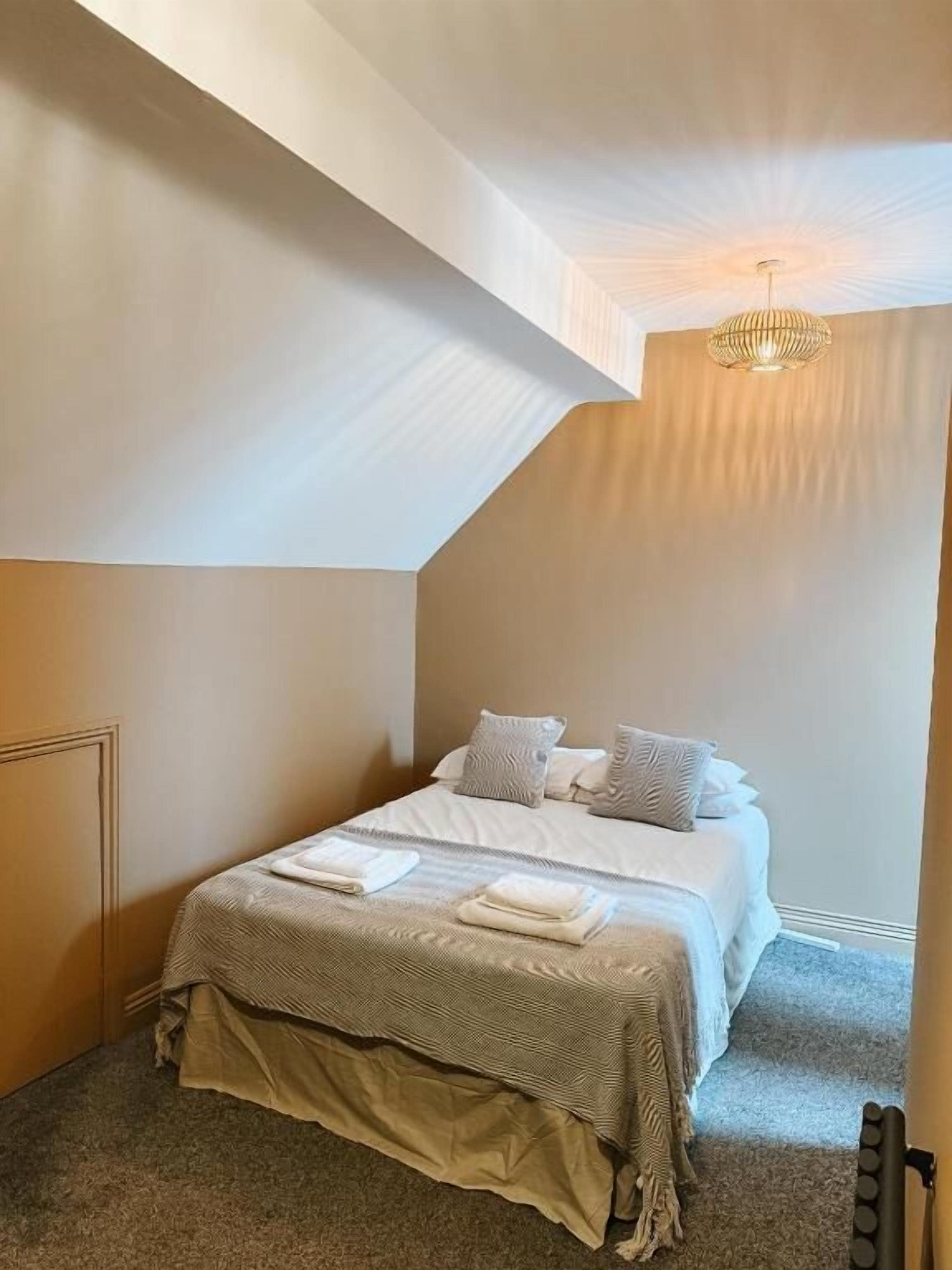 Un dormitorio con cama, almohadas, una colcha y un radiador.