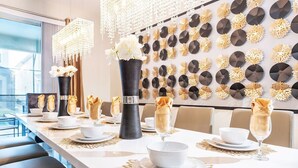 A dining area with a long table set for a meal, decorated with white flowers in vases and gold accents on the wall.