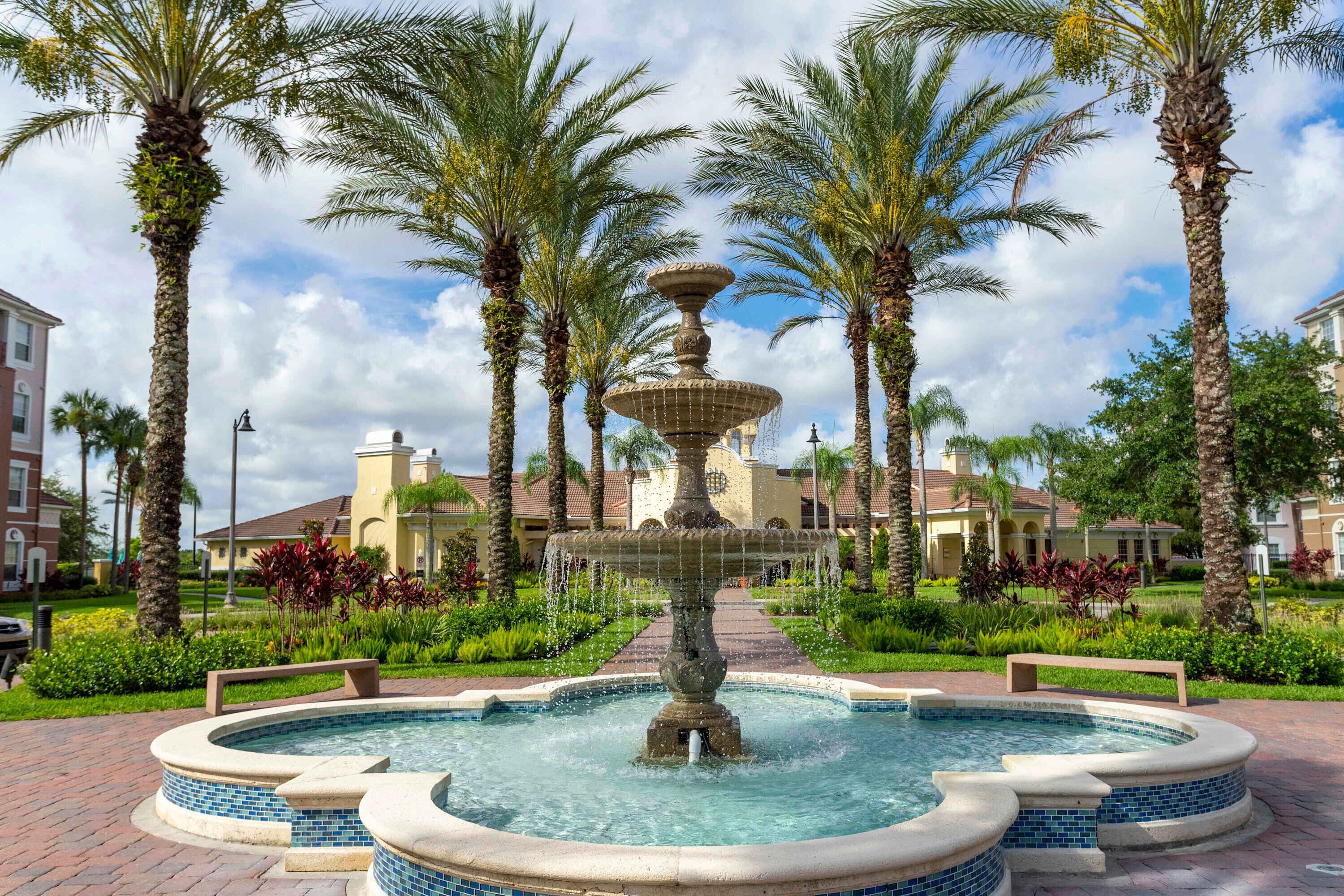 A fountain surrounded by palm trees and a brick pathway.