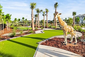 Une statue de girafe se trouve dans un espace aménagé, agrémenté de palmiers et d’un chemin sinueux.