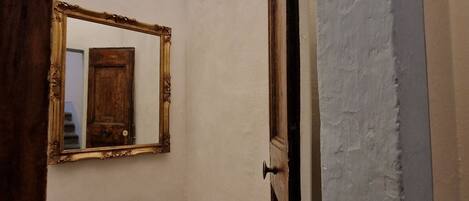 A hallway with a mirror on the wall, a wooden door, and a white wall.