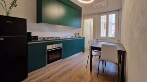 Une cuisine moderne avec des armoires de couleur turquoise, un réfrigérateur noir, une cuisinière à gaz et un coin repas comprenant une table et des chaises.
