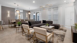 En moderne stue med en hjørnesofa, et spiseområde og en lysekrone.