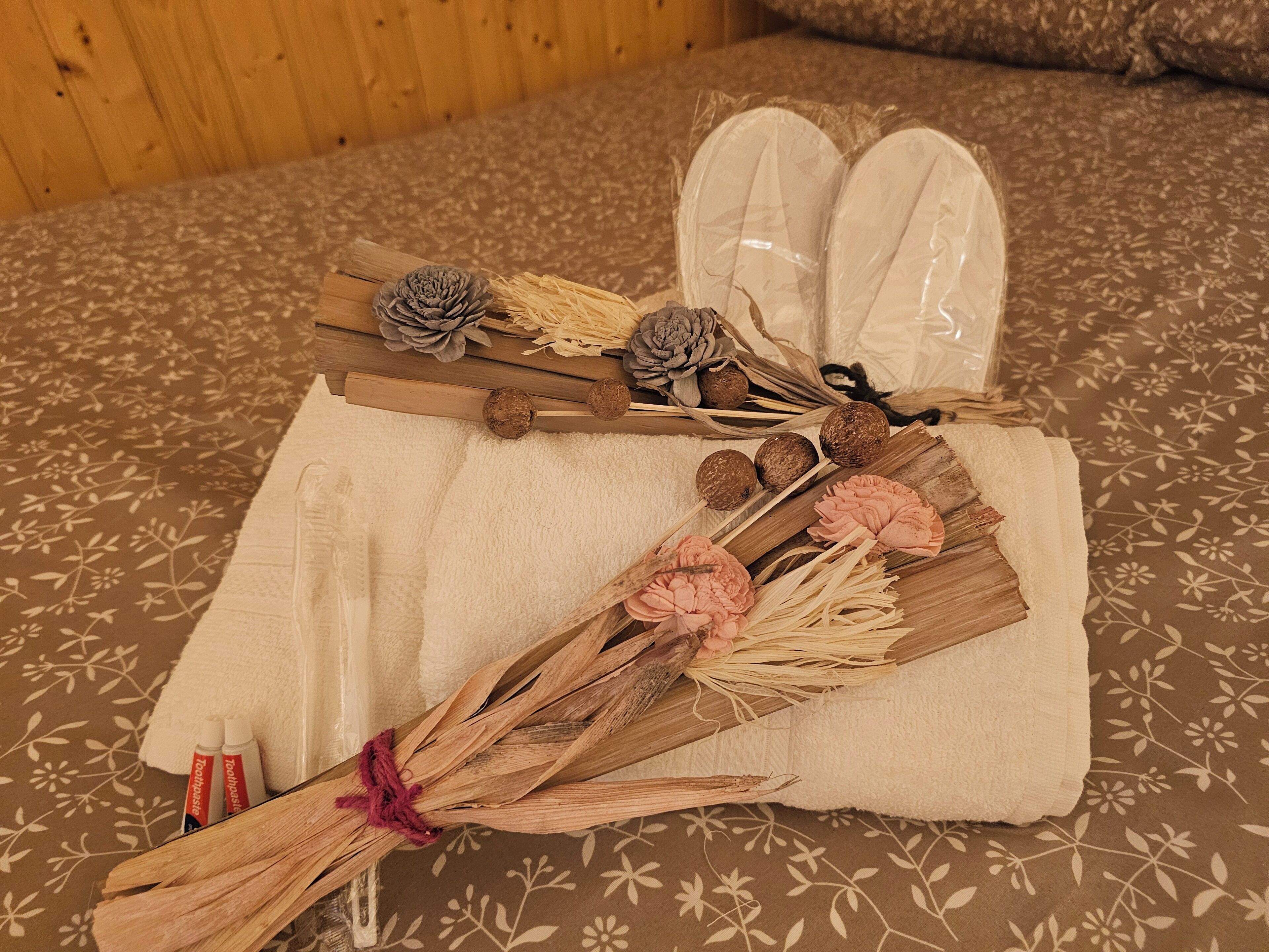 A neatly arranged bathroom with a floral-patterned towel, a pair of white slippers, and decorative items like pinecones and dried flowers.