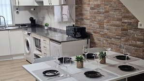 A modern kitchen with a brick wall, white cabinets, and a dining area set for four with black plates and wine glasses. - Real 43 *Good road (Neda)
