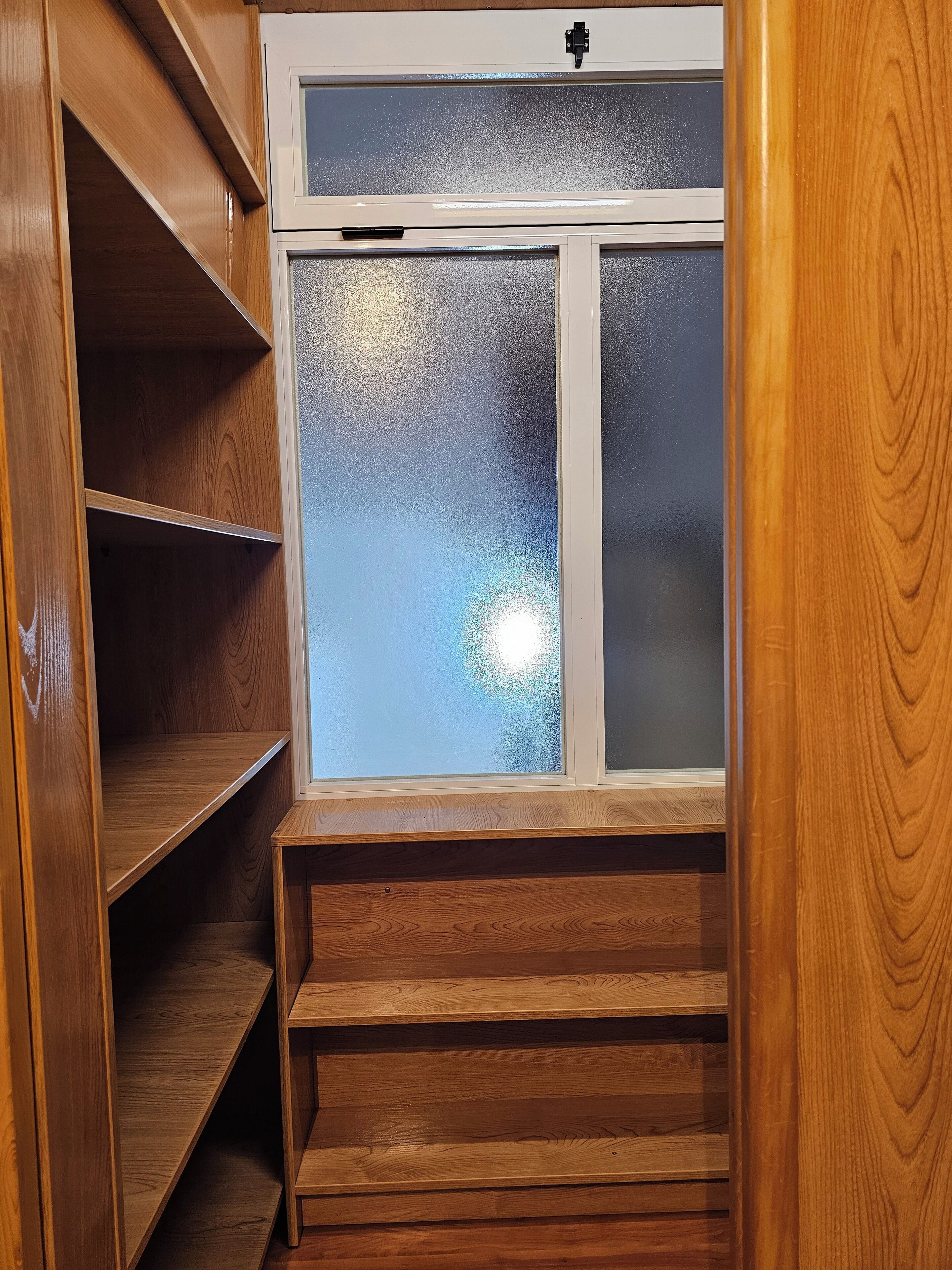 Un armadio in legno con una finestra in vetro satinato, ripiani in legno e una porta bianca.