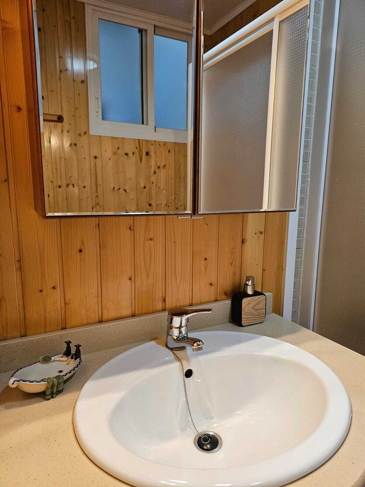 Un baño con pared de madera, un lavamanos blanco con grifo cromado y un espejo sobre el lavamanos.