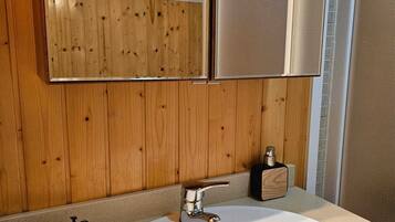 Un baño con pared de madera, un lavamanos blanco con grifo cromado y un espejo sobre el lavamanos.
