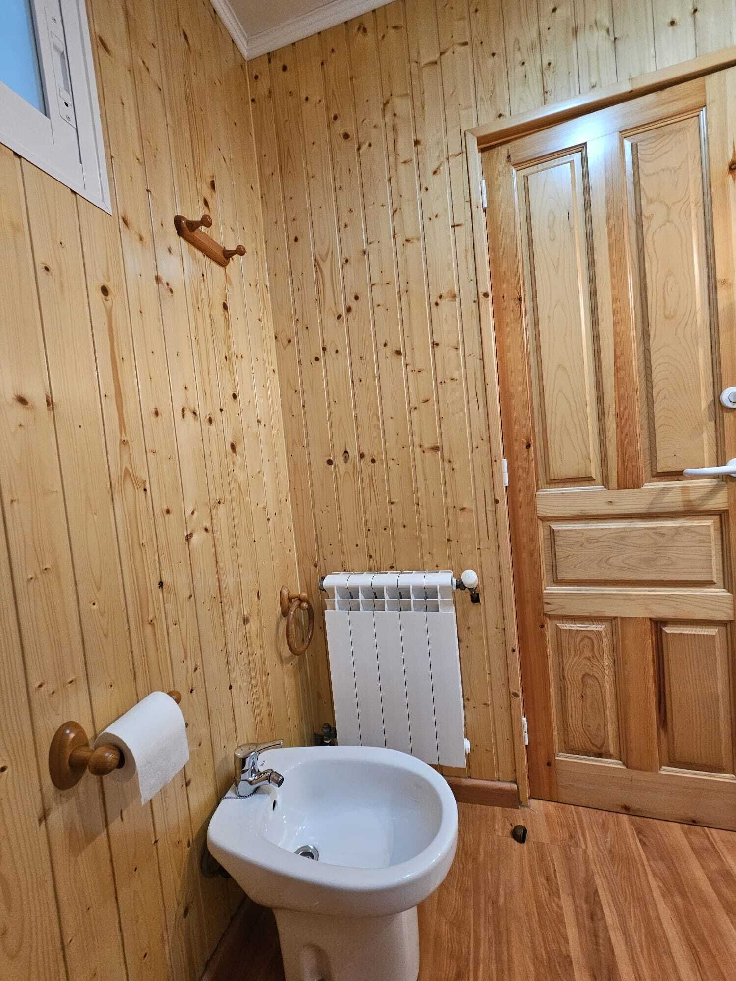 Ein Badezimmer mit Holzvertäfelung, einem weißen Waschbecken, einem Handtuchhalter und einer Heizung.