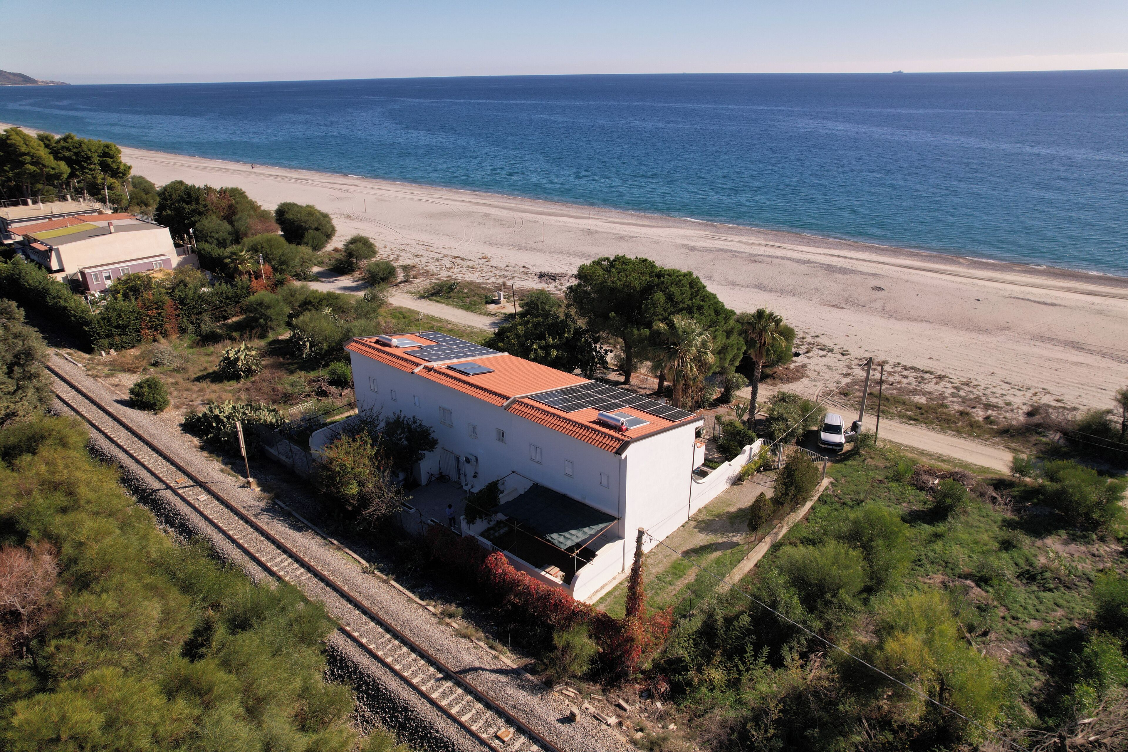 Una proprietà costiera con un edificio bianco dotato di tetto rosso, accanto a una spiaggia e a dei binari ferroviari.