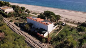 Una propiedad costera con un edificio blanco de techo rojo, junto a una playa y vías de tren.