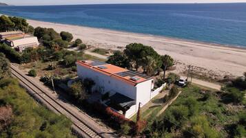 Una proprietà costiera con un edificio bianco dotato di tetto rosso, accanto a una spiaggia e a dei binari ferroviari.