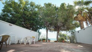 Un patio al aire libre con pared blanca, plantas en macetas y una mesa con sillas.