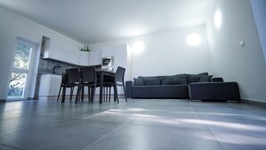 Una cocina moderna con armarios blancos, una mesa de comedor con sillas y un sofá gris.