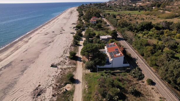 Vista aérea de una zona costera con playa, una carretera y un edificio de techo rojo cerca de la carretera.