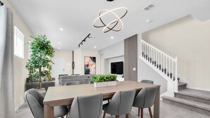 A modern dining area with a wooden table and grey upholstered chairs, a staircase, and a large potted plant.