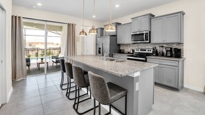 A modern kitchen with grey cabinets, a central island with bar stools, and a large window overlooking a patio.