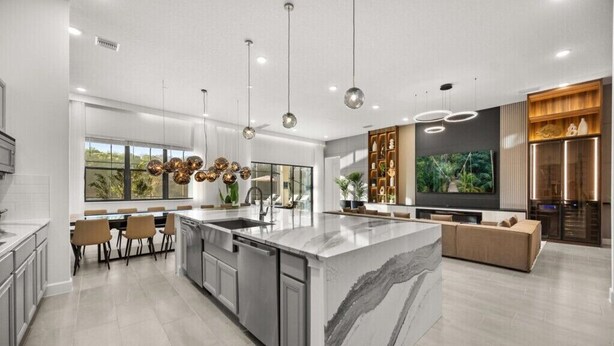 Une cuisine moderne dotée d’un grand îlot central, d’appareils électroménagers intégrés et de luminaires suspendus.