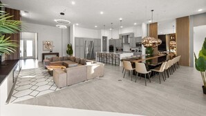 Une cuisine moderne dotée d’un îlot central, un coin repas avec une longue table et un salon avec un canapé et une table basse.