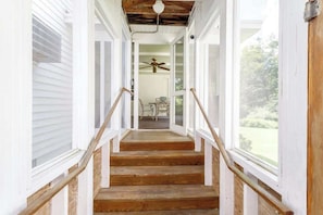 Una escalera de madera con barandillas blancas que lleva a una habitación con ventilador de techo y una mesa con sillas.