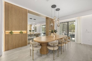 A modern dining area with a large round table, multiple chairs, hanging spherical light fixtures, and a wooden accent wall. - Last Minute Disney! Private Pool, Game Room & Themed Bedrooms. Book Now! #118059 (Orlando)