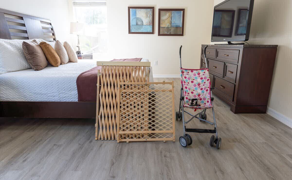 A bedroom with a bed, a wooden crib, a stroller, a dresser, and two paintings on the wall.
