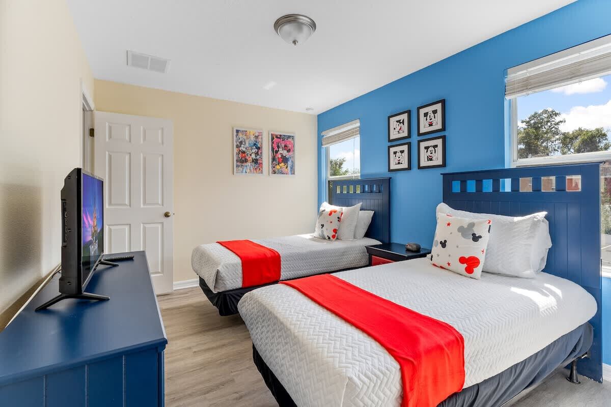 A hotel room with two beds, a TV on a stand, and artwork on the walls.