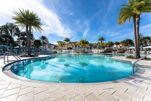 Una piscina con borde de baldosas, rodeada de palmeras y sillas de descanso.